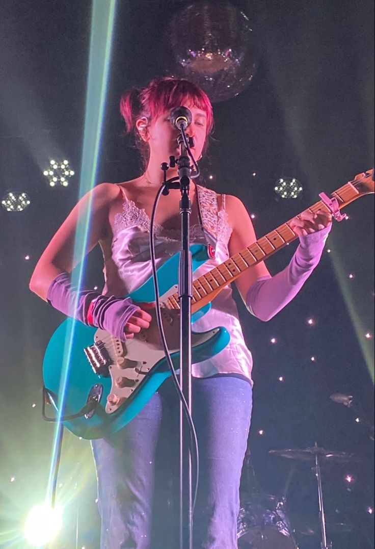 a woman standing in front of a microphone while holding a guitar