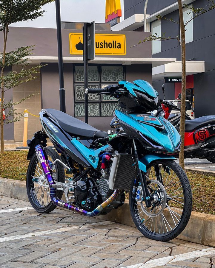 a blue motorcycle parked in front of a building on the side of a road next to a tree