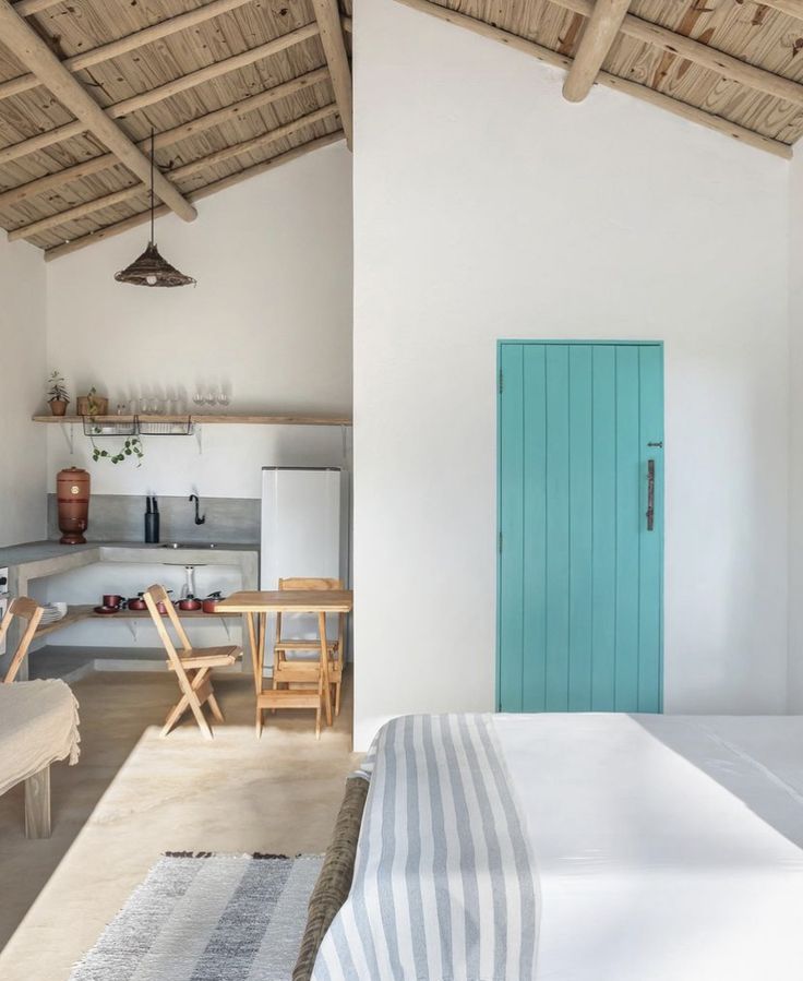 a bedroom with a bed, table and chairs in it next to a blue door