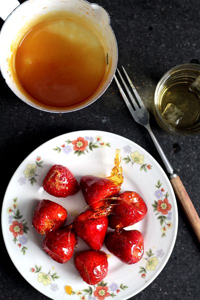 strawberries are on a plate next to a cup of tea and spoon with honey in it