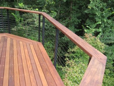 a wooden deck with metal railing and trees in the background