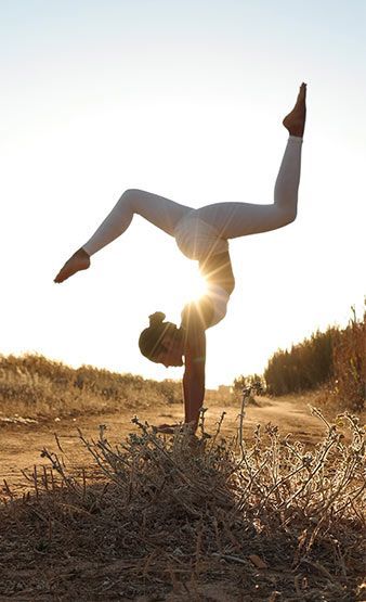 a person doing a handstand on top of a dry grass field with the sun in the background