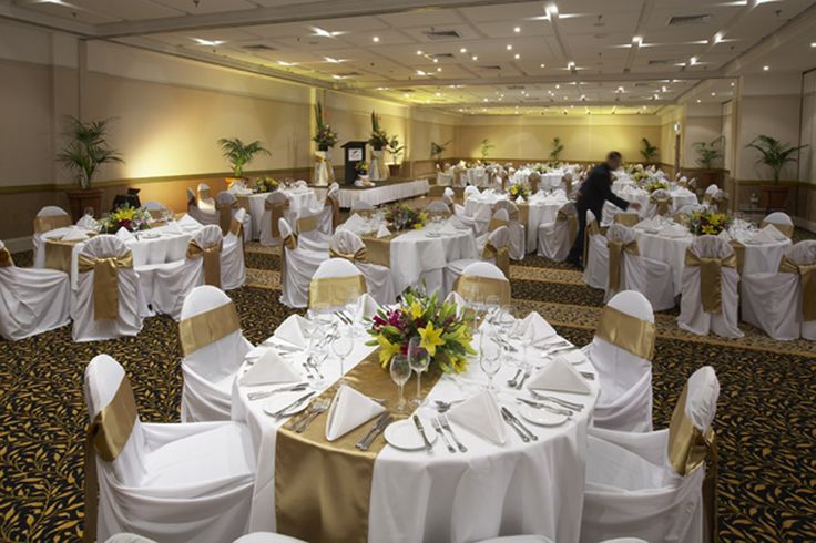 a banquet hall with tables and chairs covered in white tablecloths, gold sashers and centerpieces