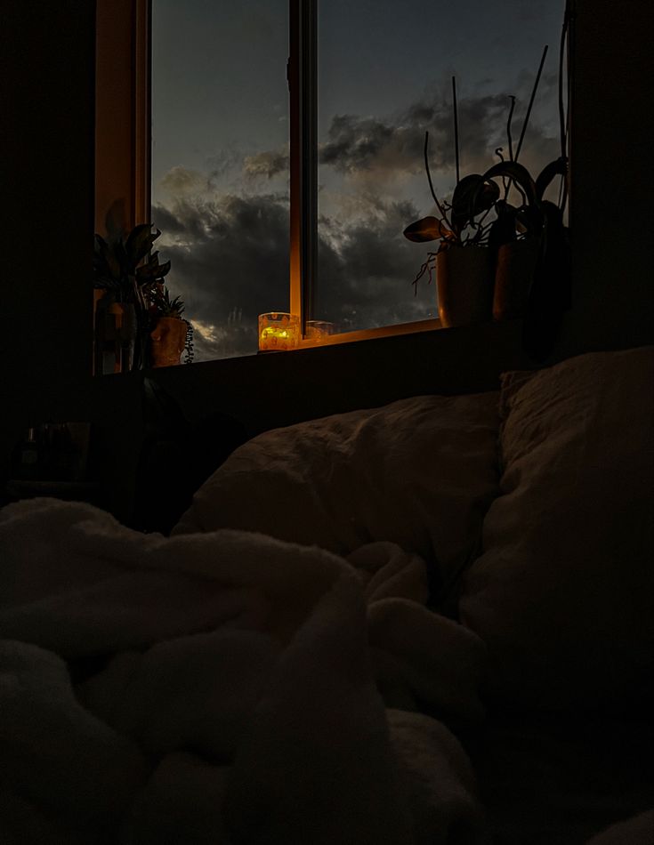 a bed sitting in front of a window under a night sky filled with white clouds