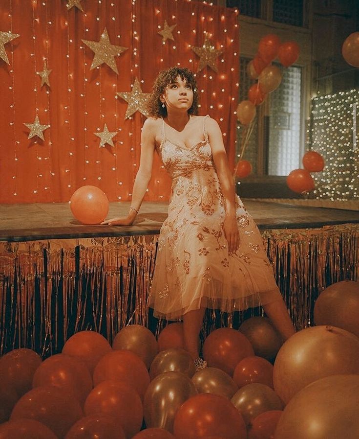 a woman in a dress standing on a stage surrounded by balloons and streamers with stars