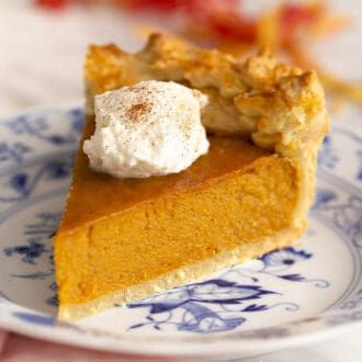 a slice of pumpkin pie on a blue and white plate with a dollop of whipped cream