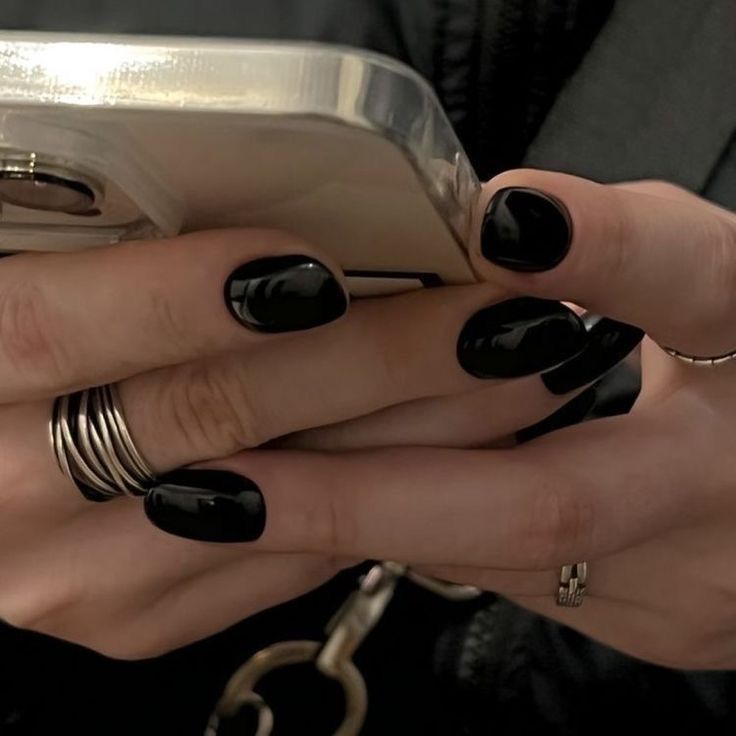 a woman with black nail polish holding a cell phone in her right hand and two rings on her left wrist