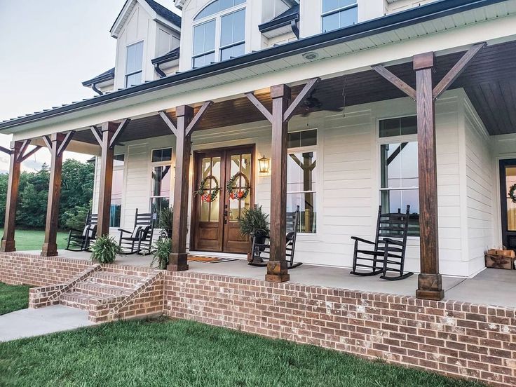 the front porch of a house with rocking chairs and wreaths hanging on it's pillars