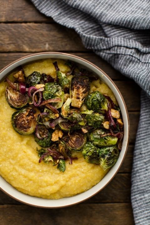 a white bowl filled with mashed potatoes and brussel sprouts on top of a wooden table