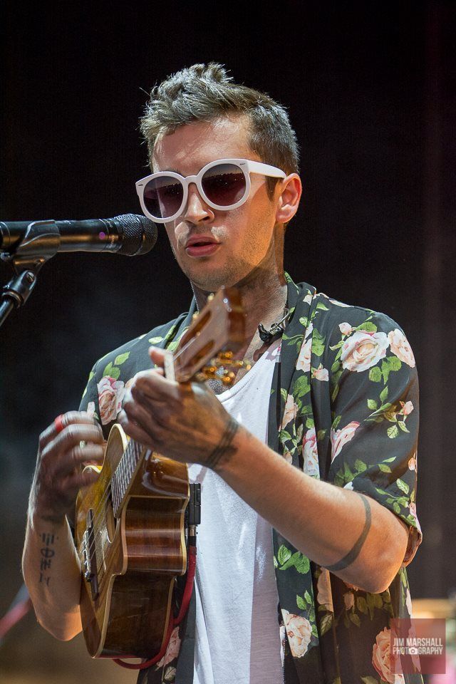 a man wearing sunglasses and holding a guitar in front of a microphone at a concert