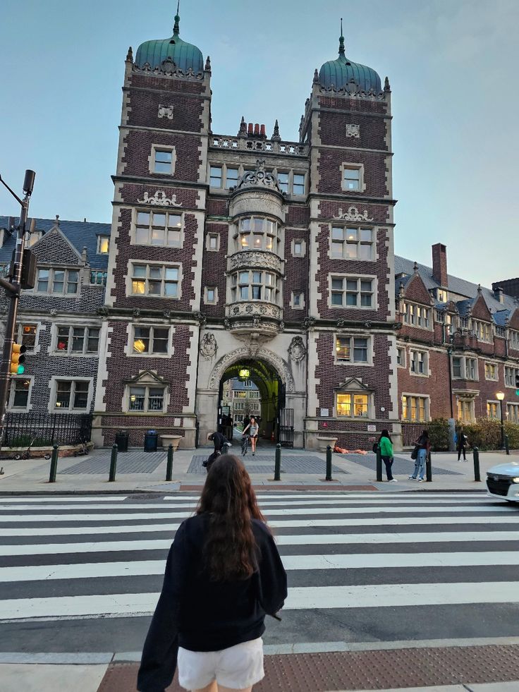 a woman walking across a cross walk in front of a large building