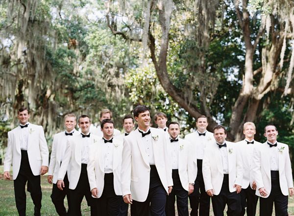 a group of men standing next to each other wearing white suits and black bow ties