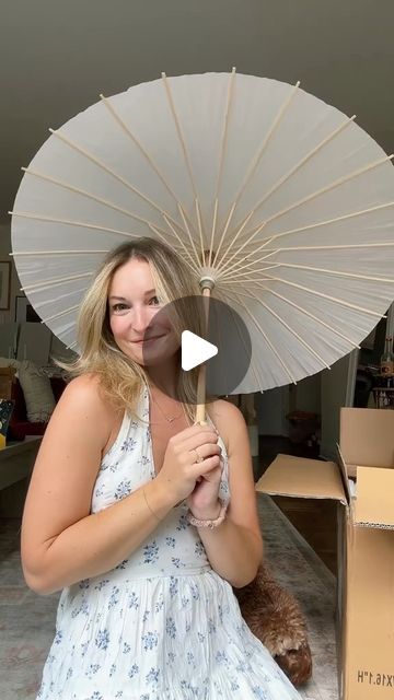 a woman holding an open umbrella in front of a cardboard box with a teddy bear