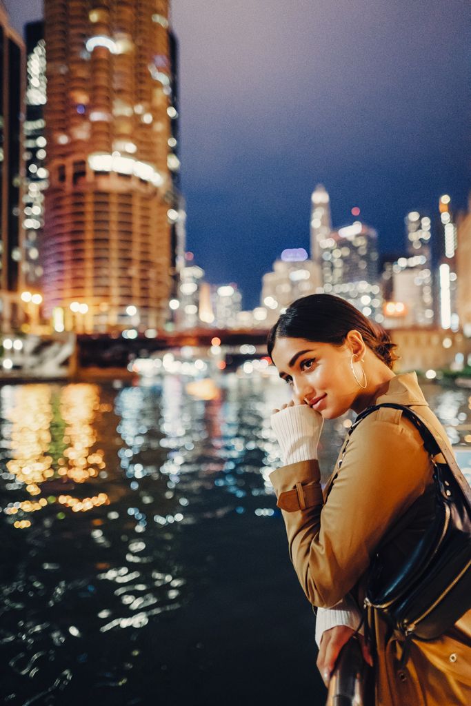 a woman standing on the edge of a river in front of a city at night