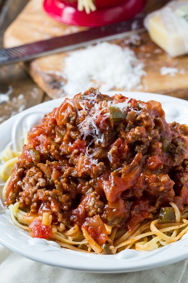 a white plate topped with spaghetti covered in meat and sauce next to bread on a cutting board