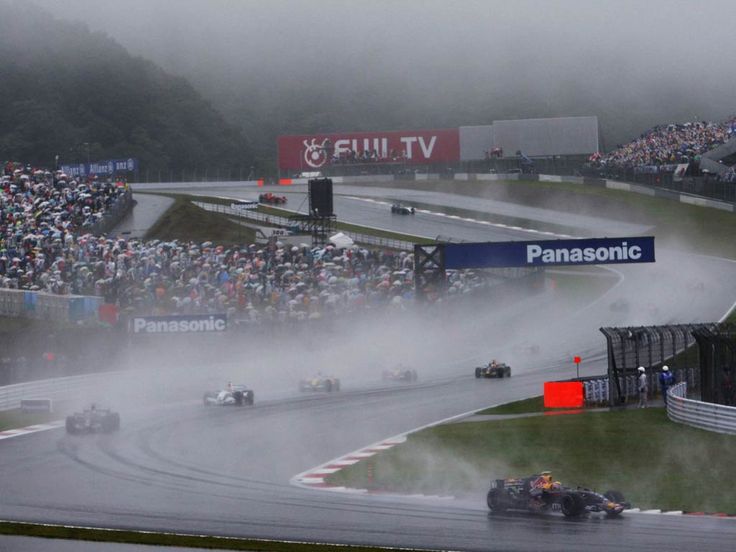 a group of cars driving down a race track with people watching from the sidelines