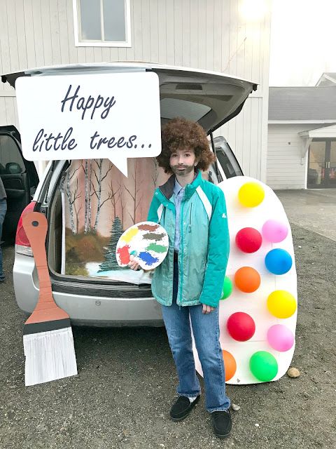 a person standing in front of a car with a sign on the back door that says happy little trees