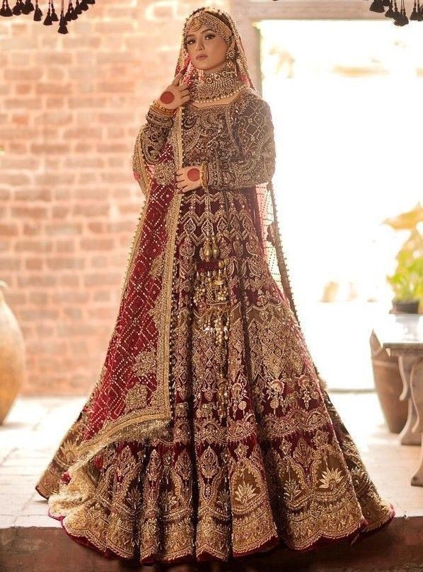 a woman in a red and gold bridal gown standing by a brick wall with chandelier