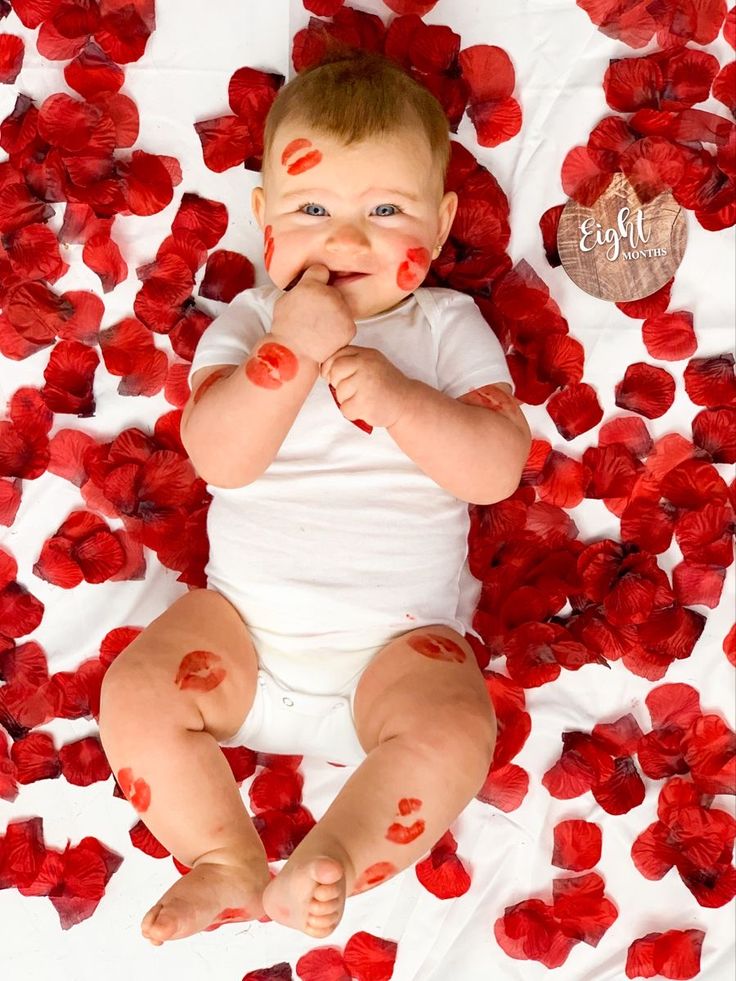 a baby with red paint all over it's face sitting on a bed of roses