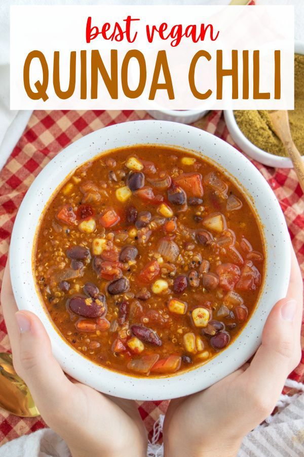 hands holding a bowl of best vegan quinoa chili on a red and white checkered tablecloth