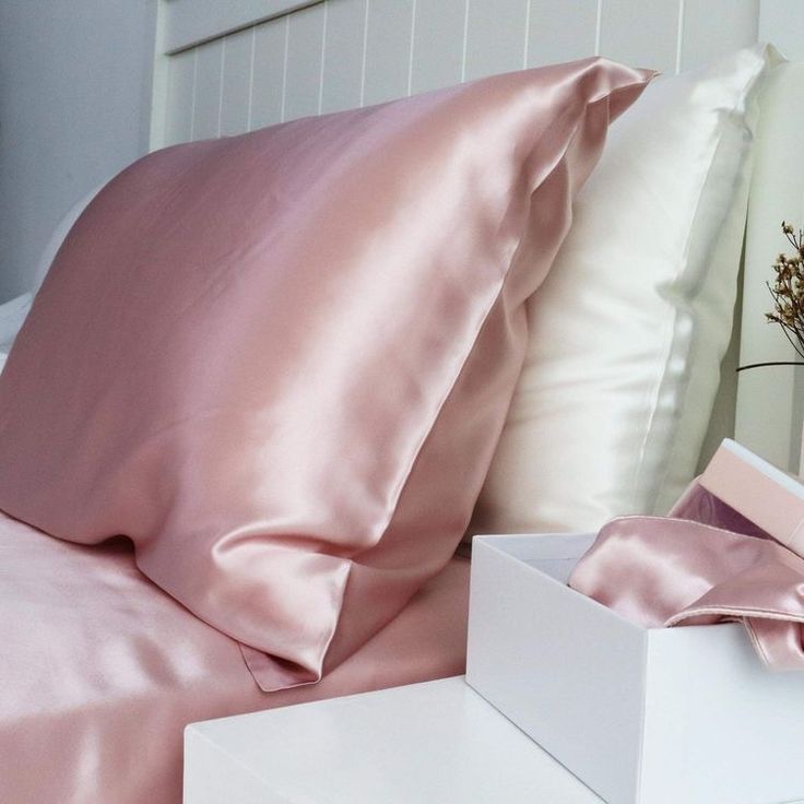 a bed with pink sheets and pillows on top of it next to a white box