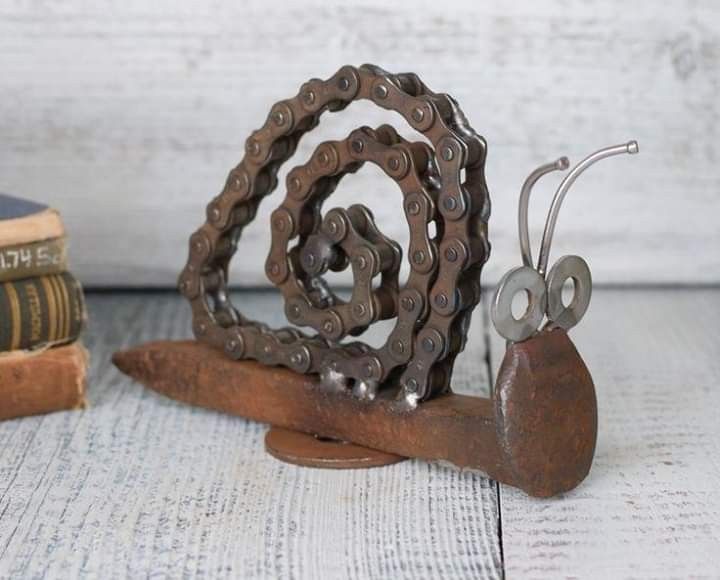 a metal snail sculpture sitting on top of a wooden table next to two old books