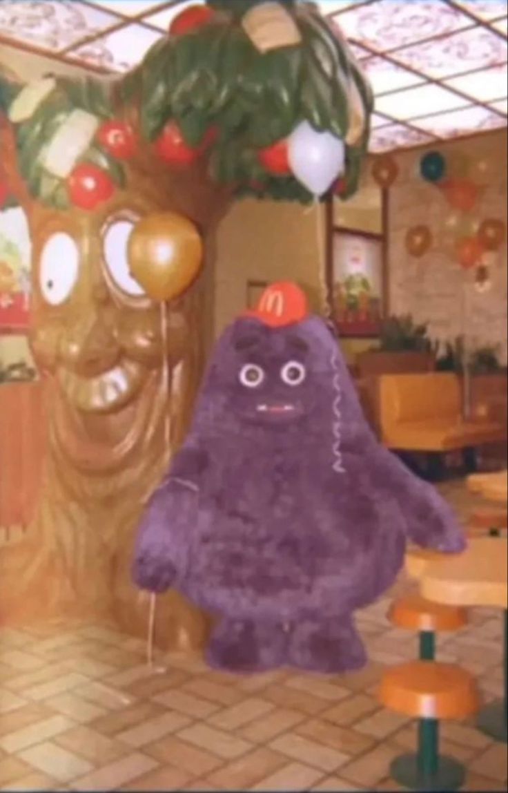 a large purple stuffed animal sitting in front of a wooden table with chairs and balloons