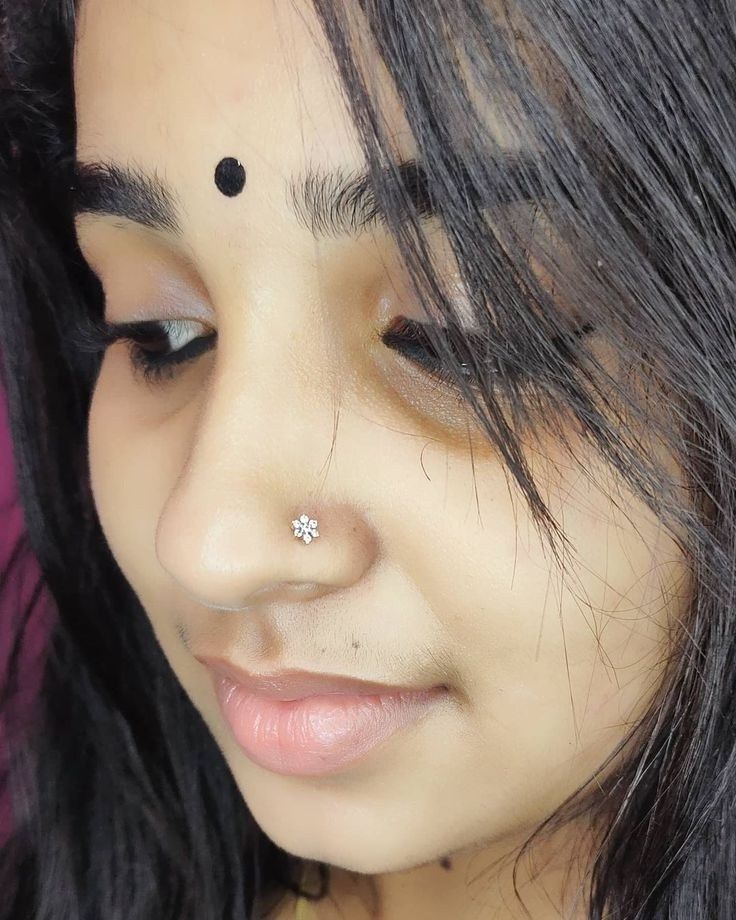 a close up of a woman with black hair and piercings on her nose looking at the camera