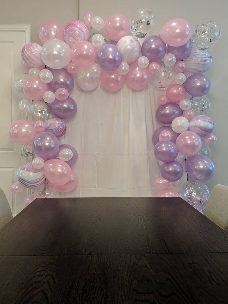 a table topped with balloons in front of a white wall and wooden tablecloths