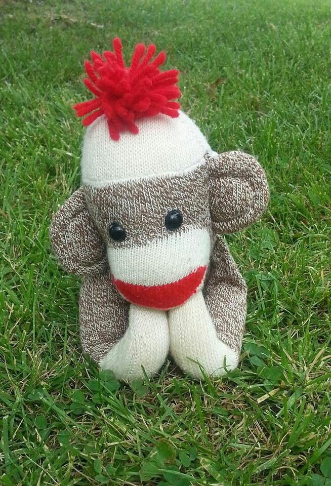 a sock monkey sitting in the grass with a red bow on it's head