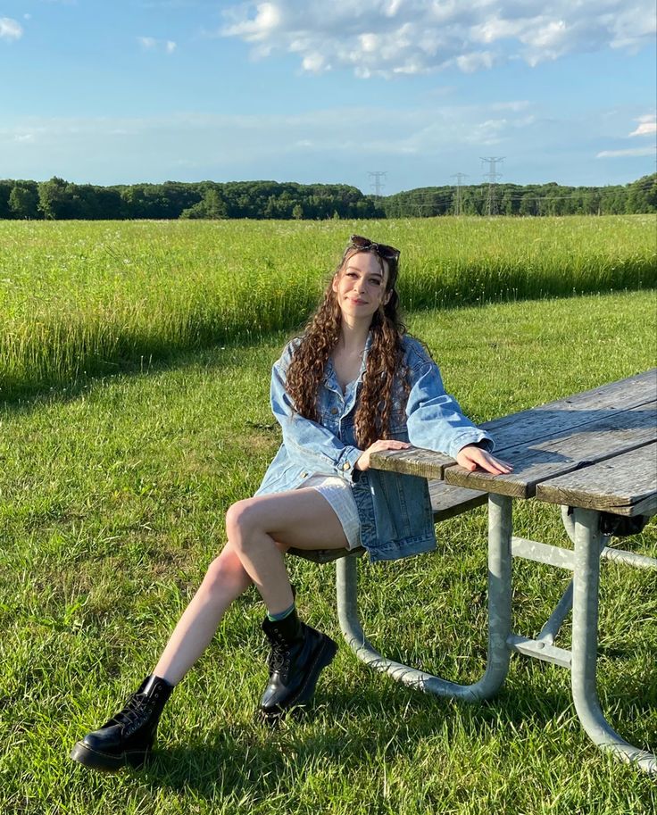 a young woman sitting at a picnic table in the middle of a grassy field with her legs crossed