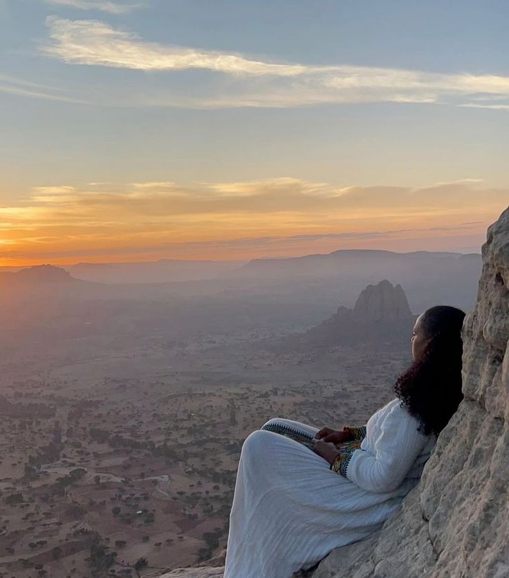 a woman sitting on top of a rock next to a mountain