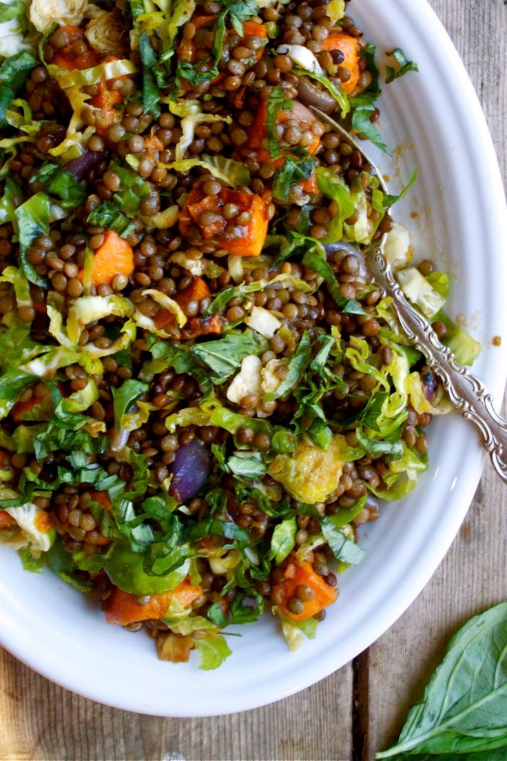 a white bowl filled with salad on top of a wooden table next to a fork