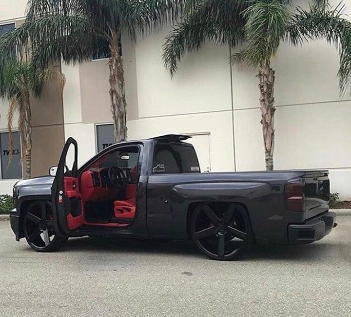 a black truck with red interior parked in front of a building next to palm trees