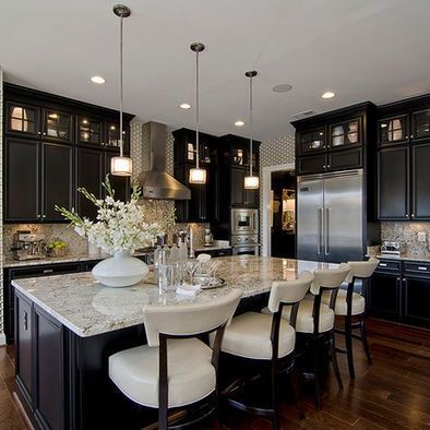 a large kitchen with black cabinets and marble counter tops, along with an island in the middle