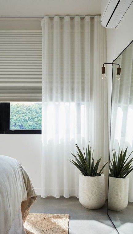 a bedroom with white curtains and plants in the corner