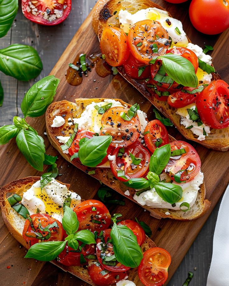 two pieces of bread with tomatoes, cheese and basil on them sitting on a cutting board