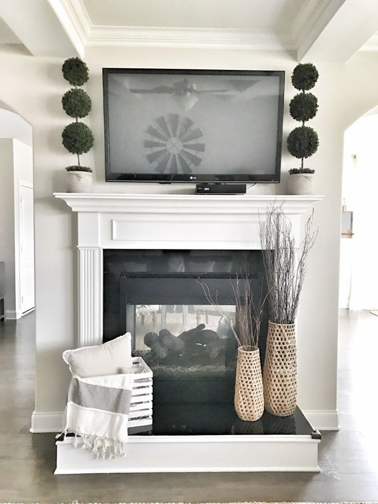 a living room with a fireplace, television and vases on top of the mantle