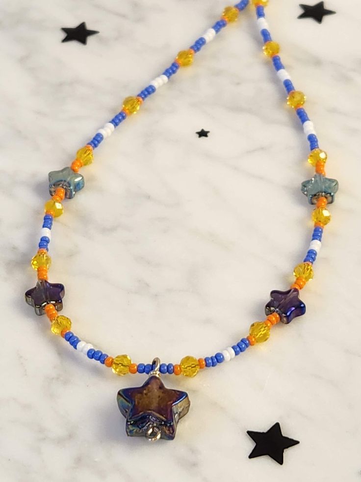 16 inch beaded star necklace arrives in ready to gift packaging. Bright yellow, orange, blue and white seed beads interspersed with small electroplated stars and a Purple carnival glass star come together for a  whimsical choker necklace. Fairy core aesthetic is perfect for a young girl or teen's birthday or for anyone who loves sparkly celestial themed jewelry. Clasp and fittings are sterling silver. Purple Star Necklace, Blue Star-shaped Jewelry With Colorful Beads, Star Charm Necklace For Festivals, Multicolor Star-shaped Adjustable Necklace, Star-shaped Beaded Necklaces For Festivals, Festival Beaded Star Necklaces, Festival Handmade Star Beaded Necklaces, Festival Star-shaped Beaded Necklace, Star-shaped Beaded Necklace For Festival