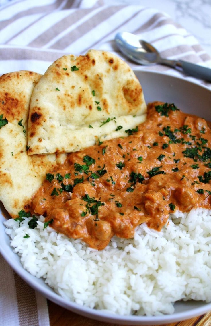 a white plate topped with rice and meat covered in sauce next to naan bread