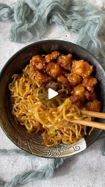 a bowl filled with noodles and chicken on top of a table next to chopsticks