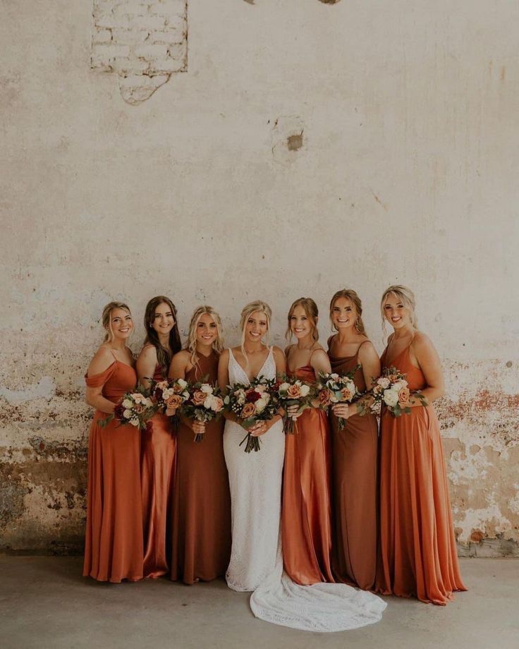 a group of women standing next to each other wearing dresses and holding bouquets in their hands