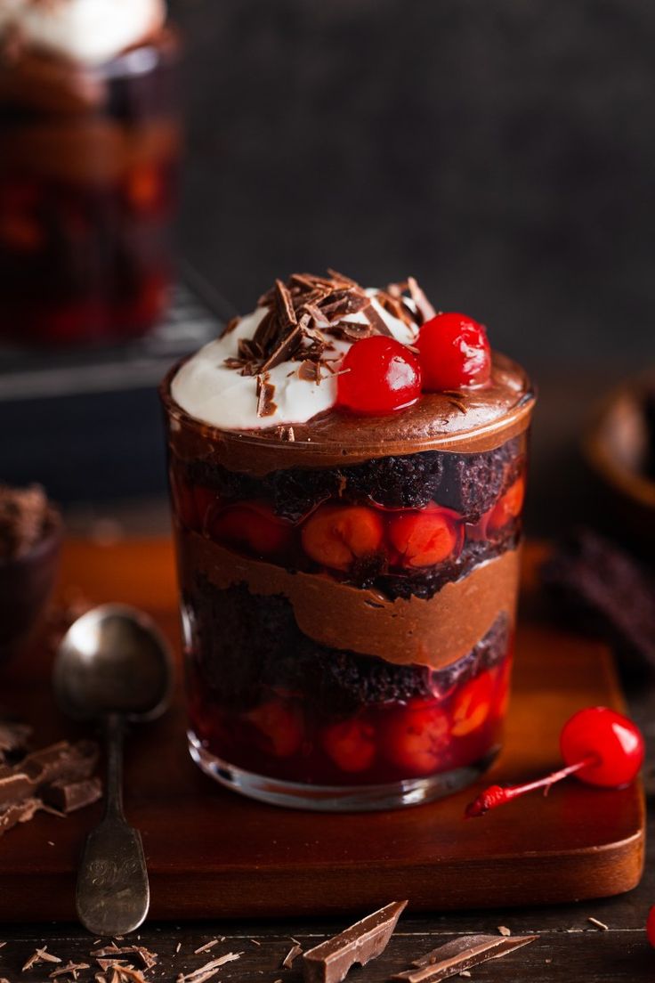 a chocolate dessert with cherries and whipped cream on top is sitting on a cutting board