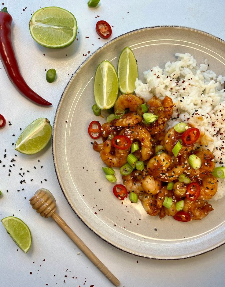 a white plate topped with rice and shrimp next to lime wedges on a table