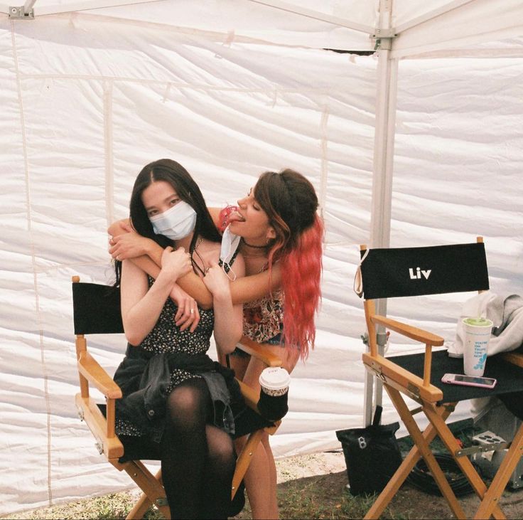 two young women sitting in chairs with their faces covered by masks while one woman holds the other