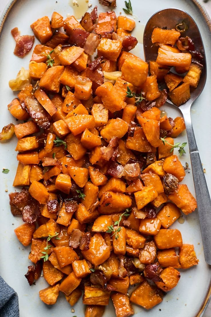 a white plate topped with sweet potatoes covered in bacon next to a spoon and fork