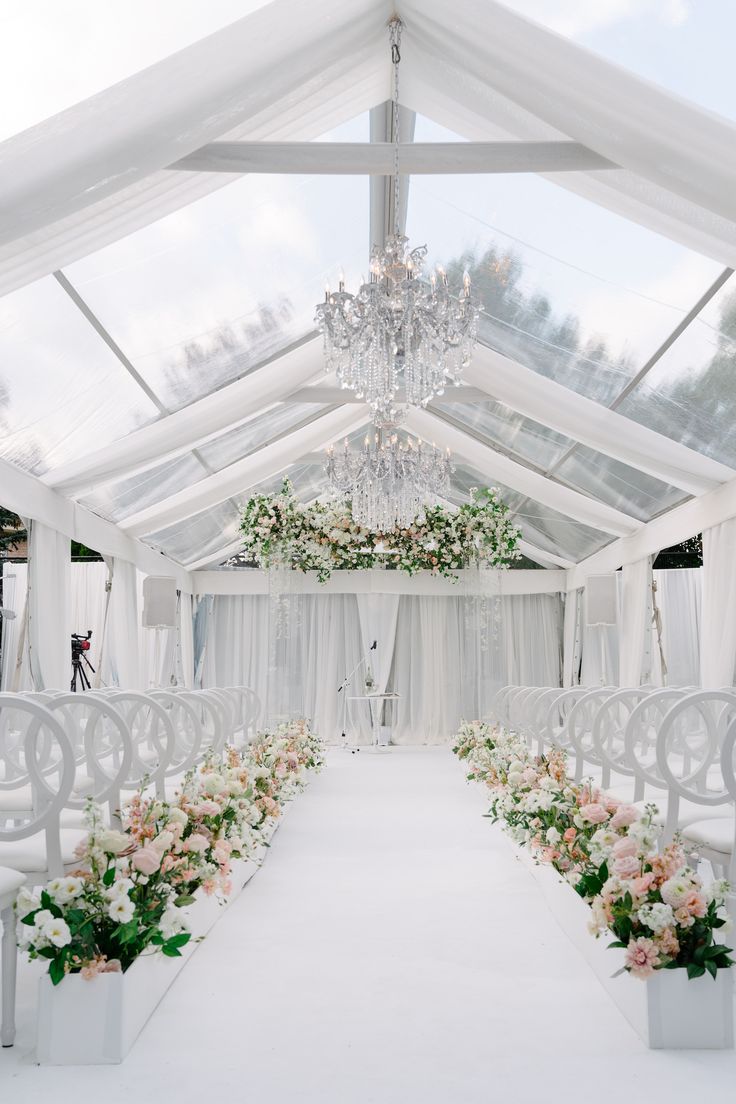 a white wedding ceremony setup with flowers and chandelier hanging from the ceiling,