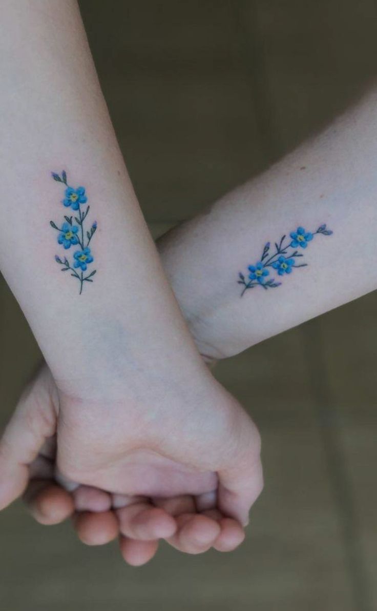 two people holding hands with small blue flowers on their wrist tattooing one another's hand