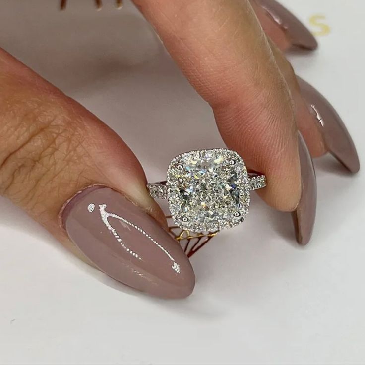 a woman's manicured nails with a ring on top of her finger and an oval shaped diamond in the middle