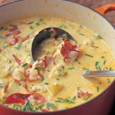 a red pot filled with soup on top of a wooden table next to a spoon